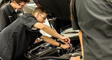 A student under the hood of a car, turning a wrench