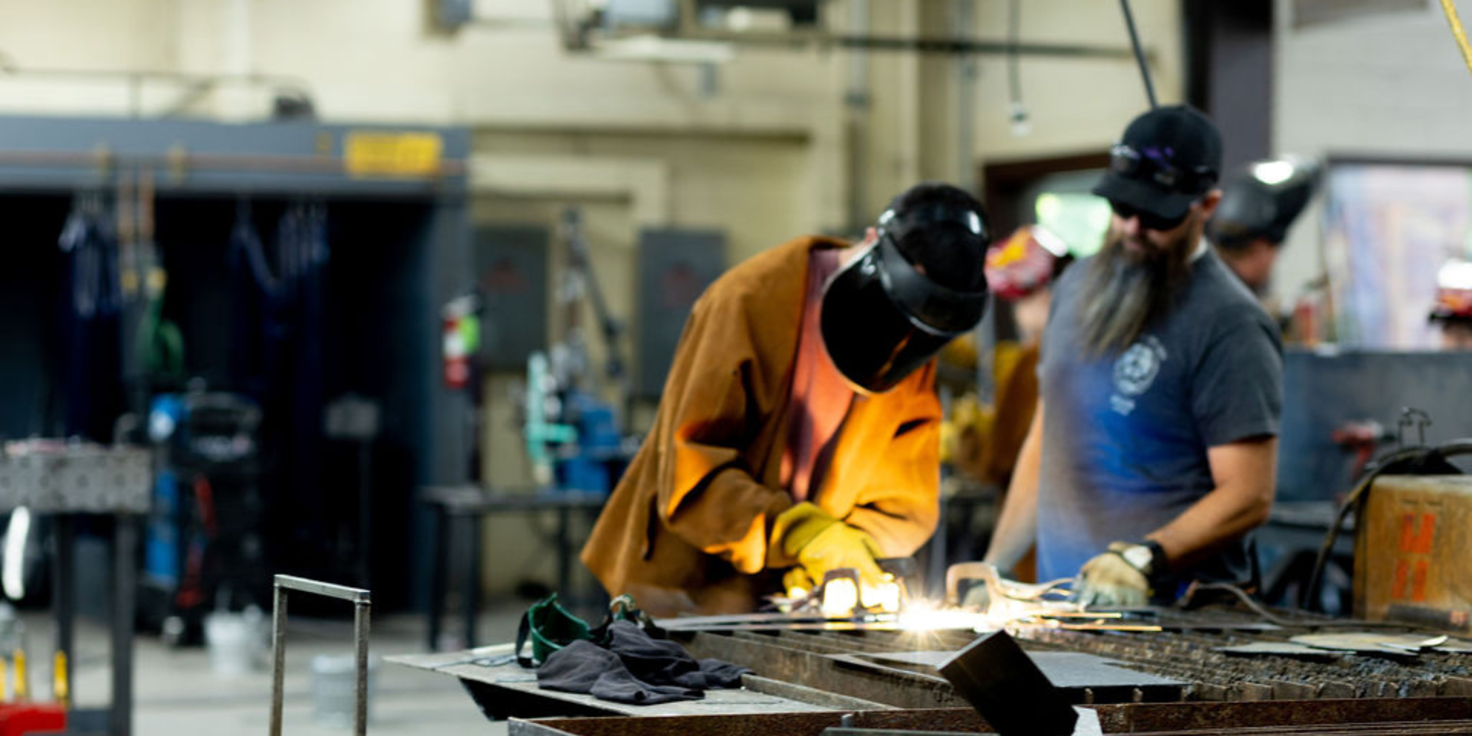 A person wearing leathers welding sheet metal, a welding hood covers their face